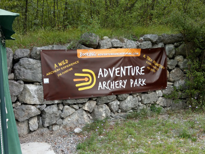 Der Banner des Adventure Archery Parks mit Beschriftung auf Englisch und Italienisch: Eine ursprüngliche Erfahrung von Bogenschießen